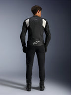 Alpinestars Dusk Airflow Leren Jas, Zwart en Wit, achteraanzicht van een rijder die een zwarte broek en laarzen draagt, voorzien van geperforeerd leer voor ventilatie, witte accordeon stretchpanelen op de schouders en witte branding op de onderrug