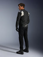 Alpinestars Dusk Airflow Leren Jas, Zwart en Wit, achteraanzicht van model die de geperforeerde leren jas draagt met bijpassende zwarte broek en laarzen, voorzien van witte accordeon stretchpanelen en een opvallend logo op de onderrug, sportieve motorrijuitrusting