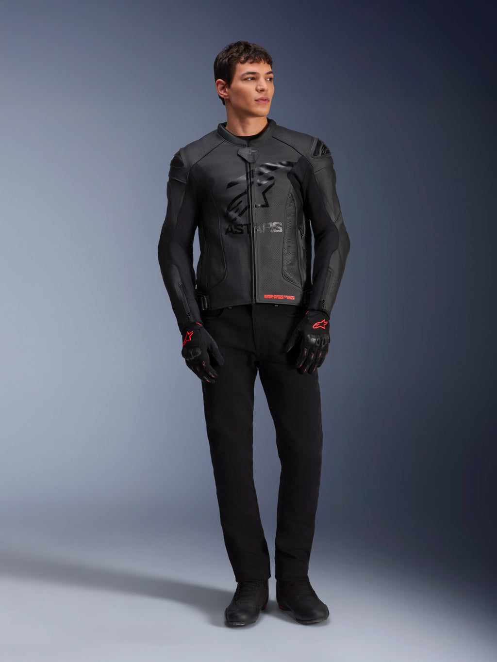 Alpinestars GP Plus R V4 Airflow leren jas, zwart, gedragen door een mannelijk model met bijpassende zwarte handschoenen en broek, voorzien van geperforeerde leren panelen, een groot tonaal sterlogo op de borst en een strakke sportieve pasvorm