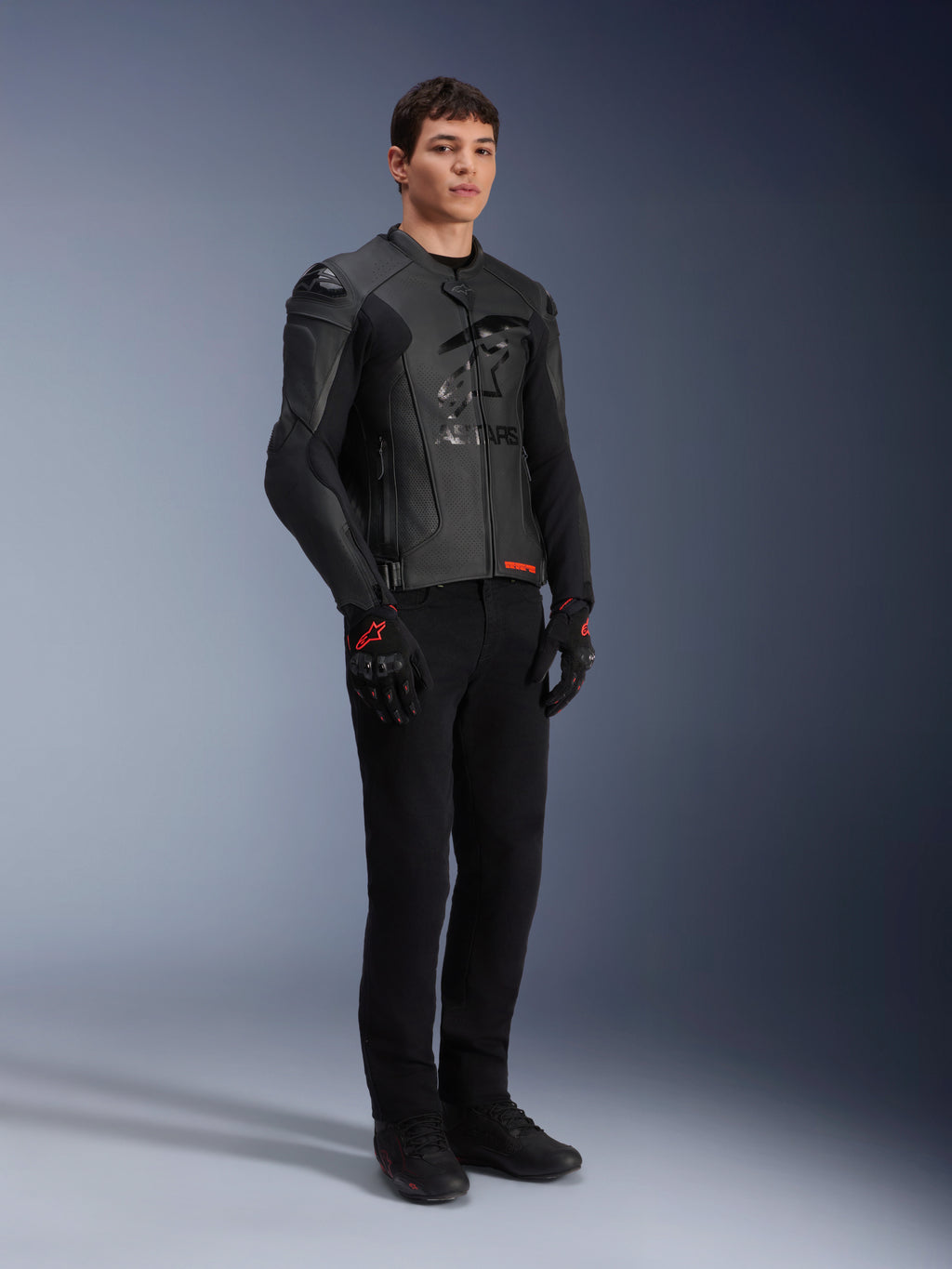 Alpinestars GP Plus R V4 Airflow leren jas, zwart, gedragen door een mannelijk model met zwarte motorbroek en handschoenen met rode accenten, voorzien van geperforeerde leren panelen en geïntegreerde schoudersliders, volledige studio-opname.