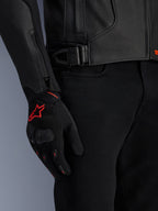 Alpinestars GP Plus R V4 Airflow leren jas, detailopname van zwart geperforeerd leer en tailleverstelling, gecombineerd met zwarte handschoenen met rode accenten en een zwarte motorbroek, professionele motoruitrusting