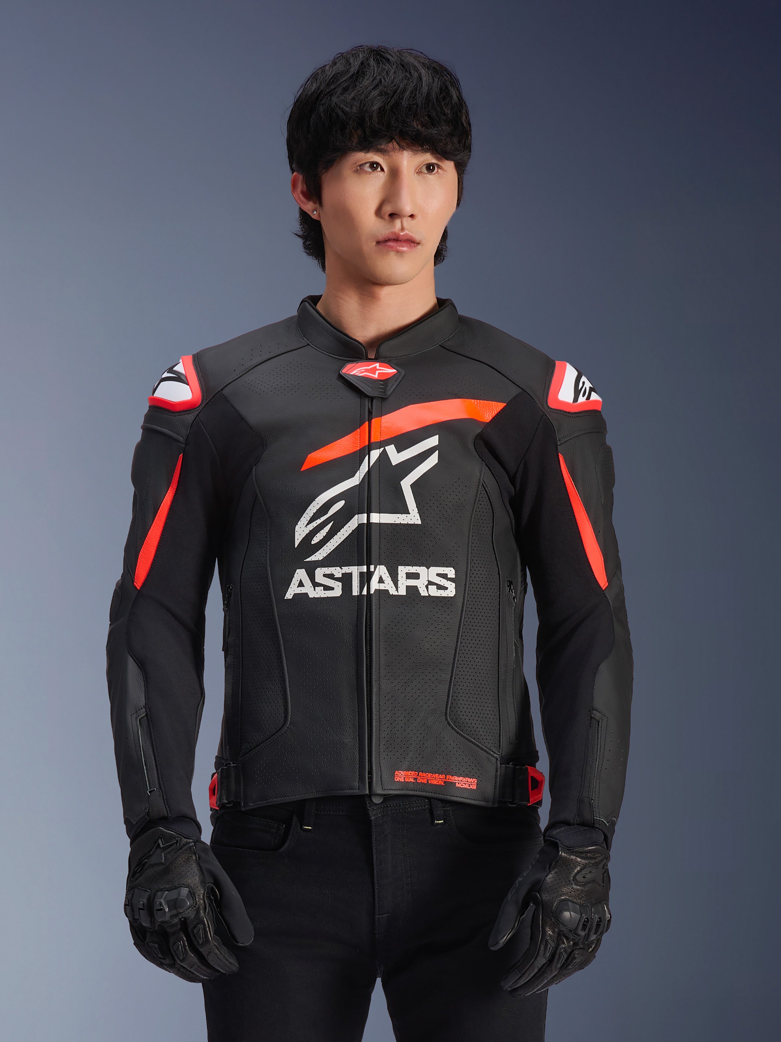 Alpinestars GP Plus R V4 Airflow motorjas, leren racingjas in zwart met rood fluo en witte accenten, gedragen door een model, met een geperforeerde leren constructie, een groot wit ASTARS-logo op de borst en geïntegreerde schouderbescherming voor motorracen