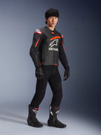 Mannelijke motorrijder in Alpinestars GP Plus R V4 Airflow Leren Jas, zwart met rood fluo en witte accenten, voorzien van geperforeerd leer en ASTARS-logo op de borst, gedragen met zwarte motorbroek en zwarte motorlaarzen, sportieve performance kleding