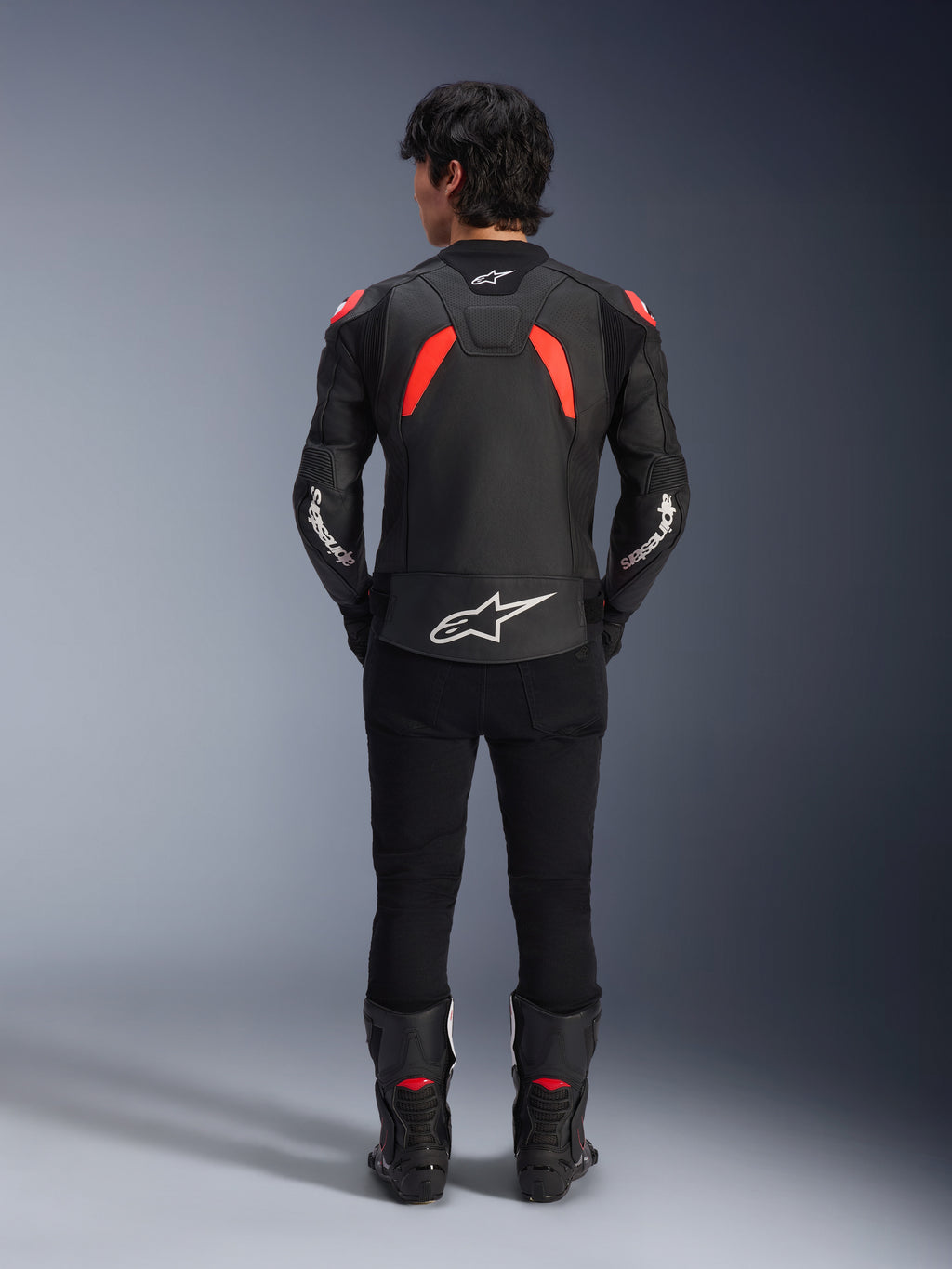 Alpinestars GP Plus R V4 Airflow lederen jas, zwart, fluo rood en wit, achteraanzicht op een model, voorzien van geperforeerde leren panelen en opvallende witte logo's, gecombineerd met een zwarte motorbroek en laarzen