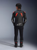 Alpinestars GP Plus R V4 Airflow lederen jas, zwart, fluo rood en wit, achteraanzicht op een model, voorzien van geperforeerde leren panelen en opvallende witte logo's, gecombineerd met een zwarte motorbroek en laarzen