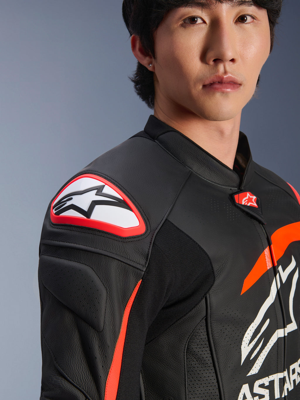 Alpinestars GP Plus R V4 Airflow lederen jas, zwart rood fluo wit, close-up van een model dat de jas draagt, met een opvallend Astar-logo op de schouderslider en geperforeerd leer op de borst voor maximale luchtstroom, professionele motorsportkleding