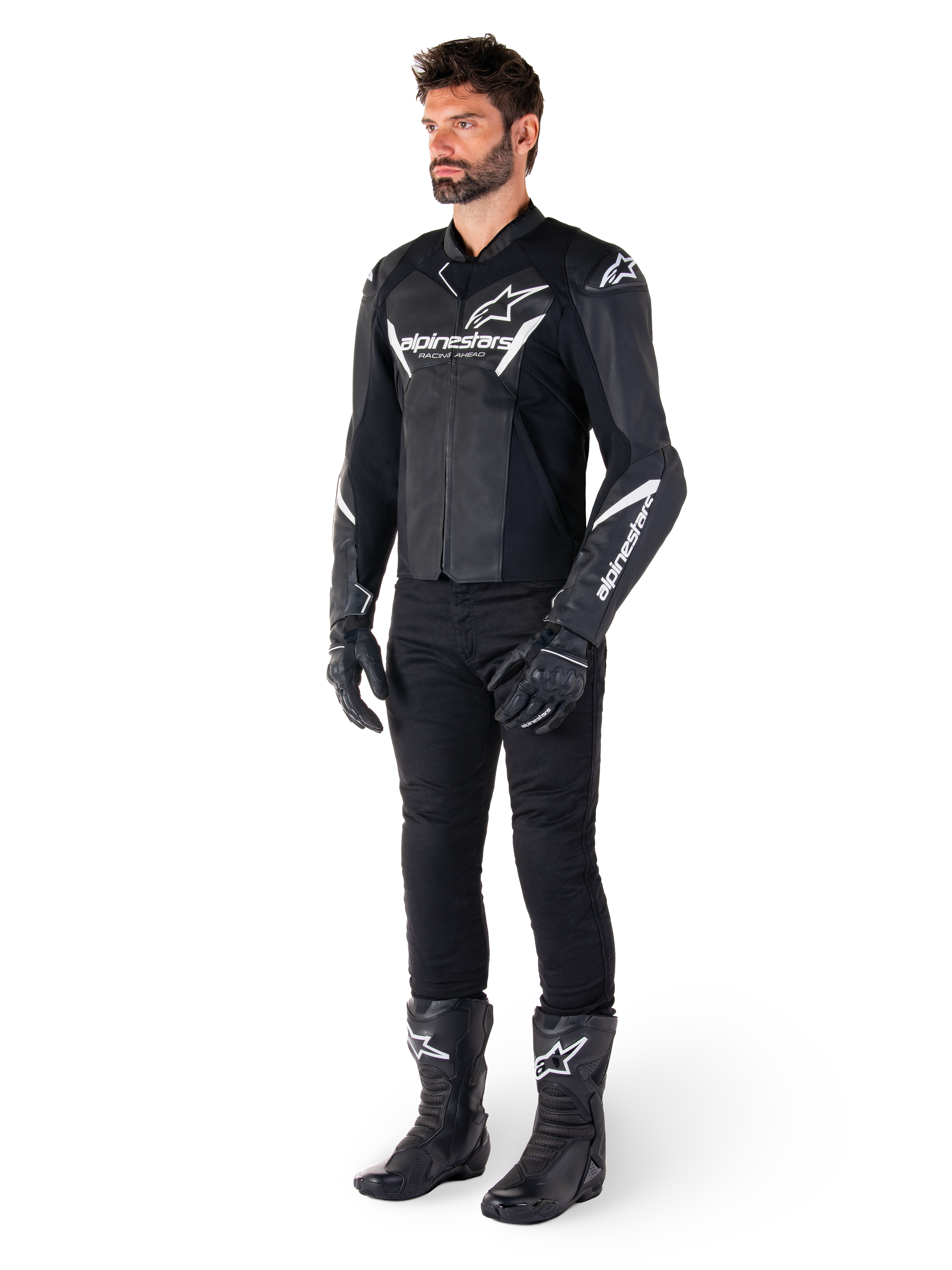 Mannelijk model draagt Alpinestars Faster V3 Leather Jacket, sportieve leren motorjas, zwart en wit, gecombineerd met zwarte motorbroek, handschoenen en laarzen, voorzien van witte branding en logo's, sportieve pasvorm voor wegracen