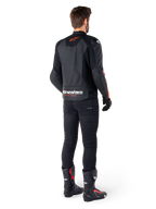 Alpinestars Faster V3 Airflow leren jas, zwart en rood fluo, van achteren gezien op een rijder, met geperforeerde leren panelen en opvallende branding, gedragen met zwarte broek en motorlaarzen, sportieve motoruitrusting.