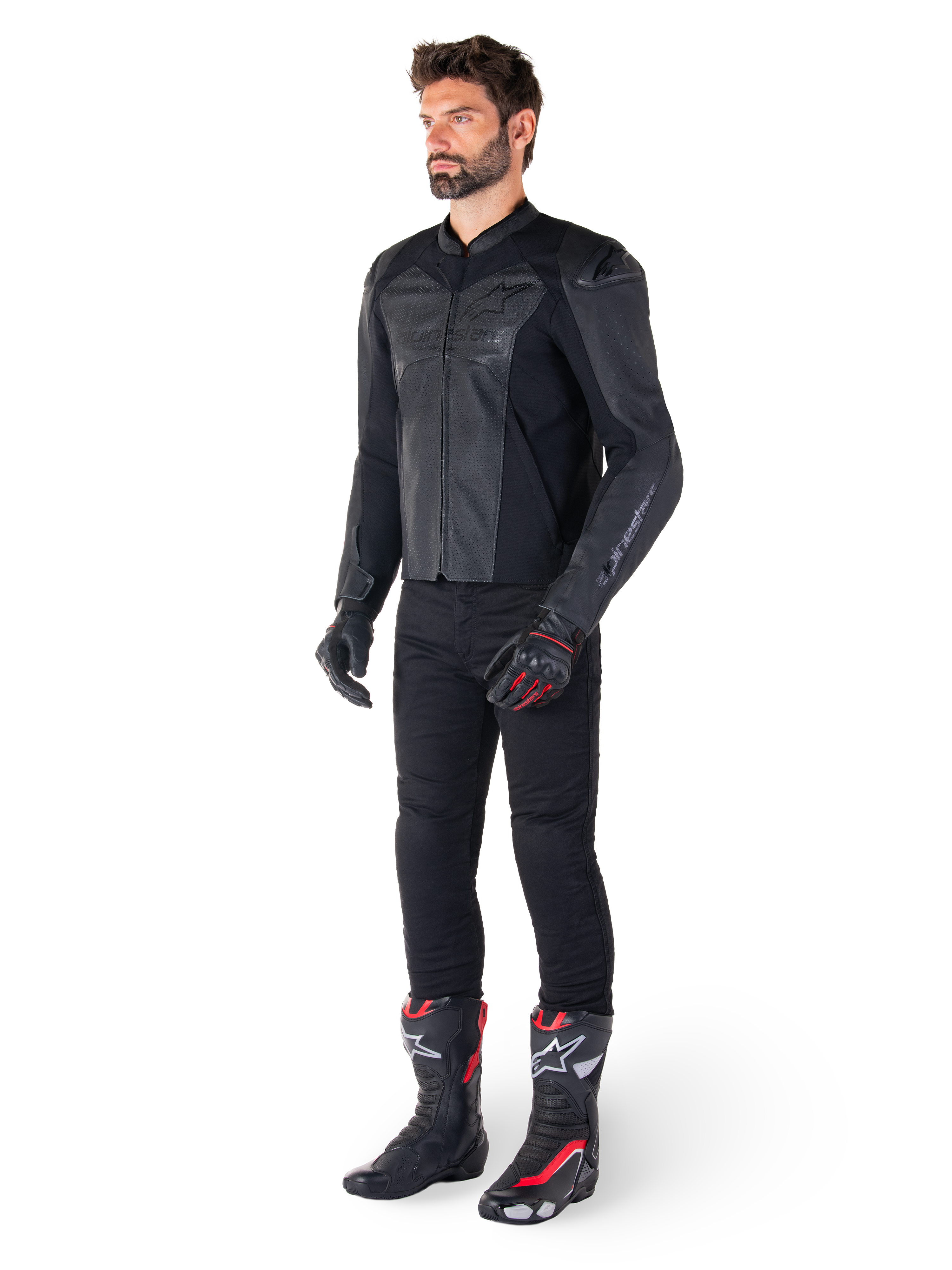 Man die Alpinestars Faster V3 Airflow leren jas in Black Black draagt, gecombineerd met een zwarte broek, zwart-rode motorhandschoenen en zwarte racelaarzen met rode en witte accenten, volledige sportieve motoruitrusting