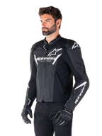 Alpinestars Faster V3 Airflow Leren Jas, zwart en wit, sportieve motorjas met geperforeerde leren panelen, witte Alpinestars-branding op de borst en mouwen, gedragen door een model met zwarte handschoenen en broek, strakke en beschermende rijuitrusting