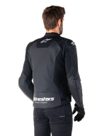 Alpinestars Faster V3 Airflow Leren Jas, zwart en wit, achteraanzicht op een model, geperforeerd lederen rugpaneel voor ventilatie, witte Astars-logo's op de bovenrug en onderrug met 'Racing Ahead'-tekst, sportief ontwerp met stretchpanelen voor motorrijden.