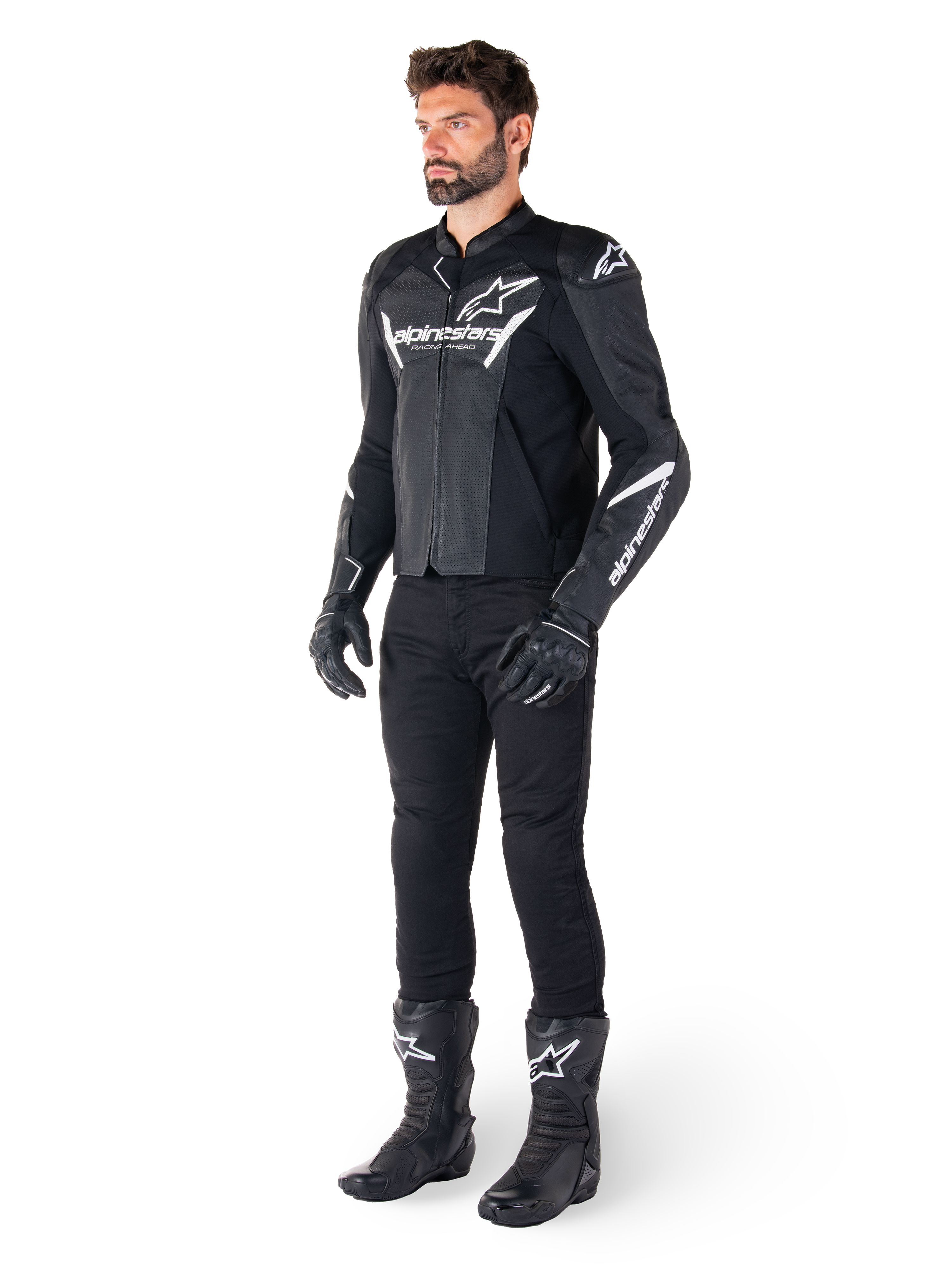 Model draagt Alpinestars Faster V3 Airflow Leren Jas, zwart en wit, voorzien van geperforeerd leer en witte Alpinestars-logo's, gecombineerd met een zwarte motorbroek, handschoenen en laarzen, sportieve motoruitrusting