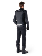 Alpinestars Faster V3 Airflow leren jas, zwart en wit, achteraanzicht met geperforeerde leren panelen en opvallende Alpinestars-branding op de onderrug, gedragen door een motorrijder met zwarte motorbroek, handschoenen en laarzen