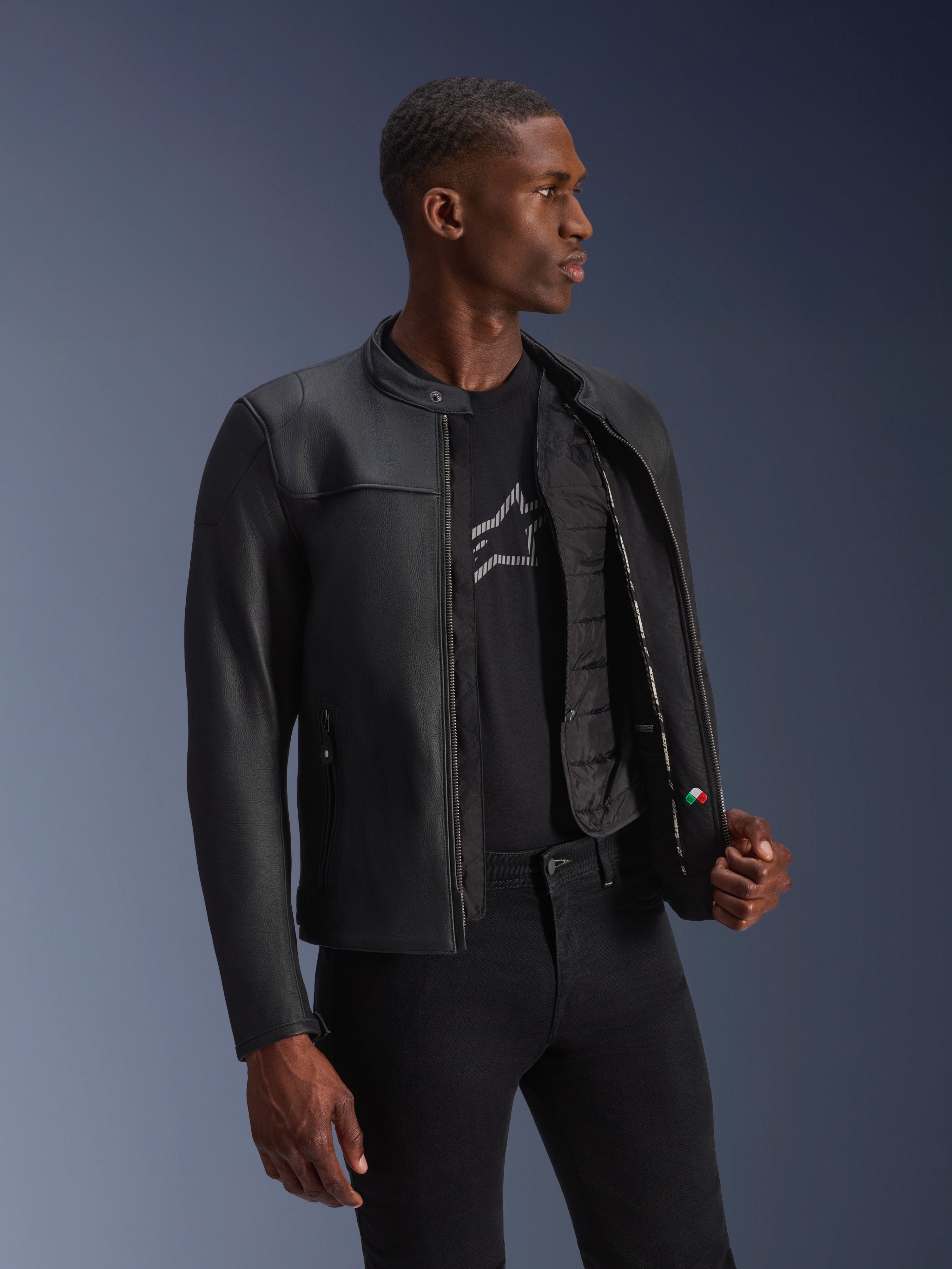 Alpinestars Blacktrack Leren Jas, zwart, premium rundleer met een op maat gemaakte pasvorm, opengeritst om het afneembare thermische vest en de interieurdetails te tonen, gedragen door een model, moderne urban motorkleding