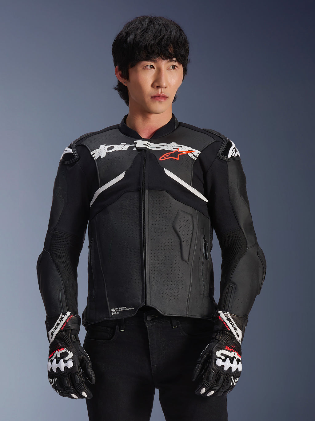 Alpinestars Atem V5 leren motorjas, motorracejas, zwart met witte en rode accenten, hoogwaardige leren constructie met bepantserde bescherming, gedragen met bijpassende racehandschoenen
