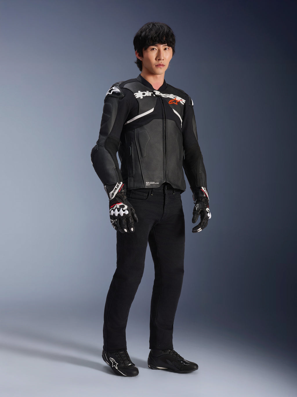 Alpinestars Atem V5 Leren Jas, motorracejas, zwart en wit, gedragen met een zwarte broek en bijpassende handschoenen, met witte Alpinestars-branding op de borst en beschermende schouderprotectie.