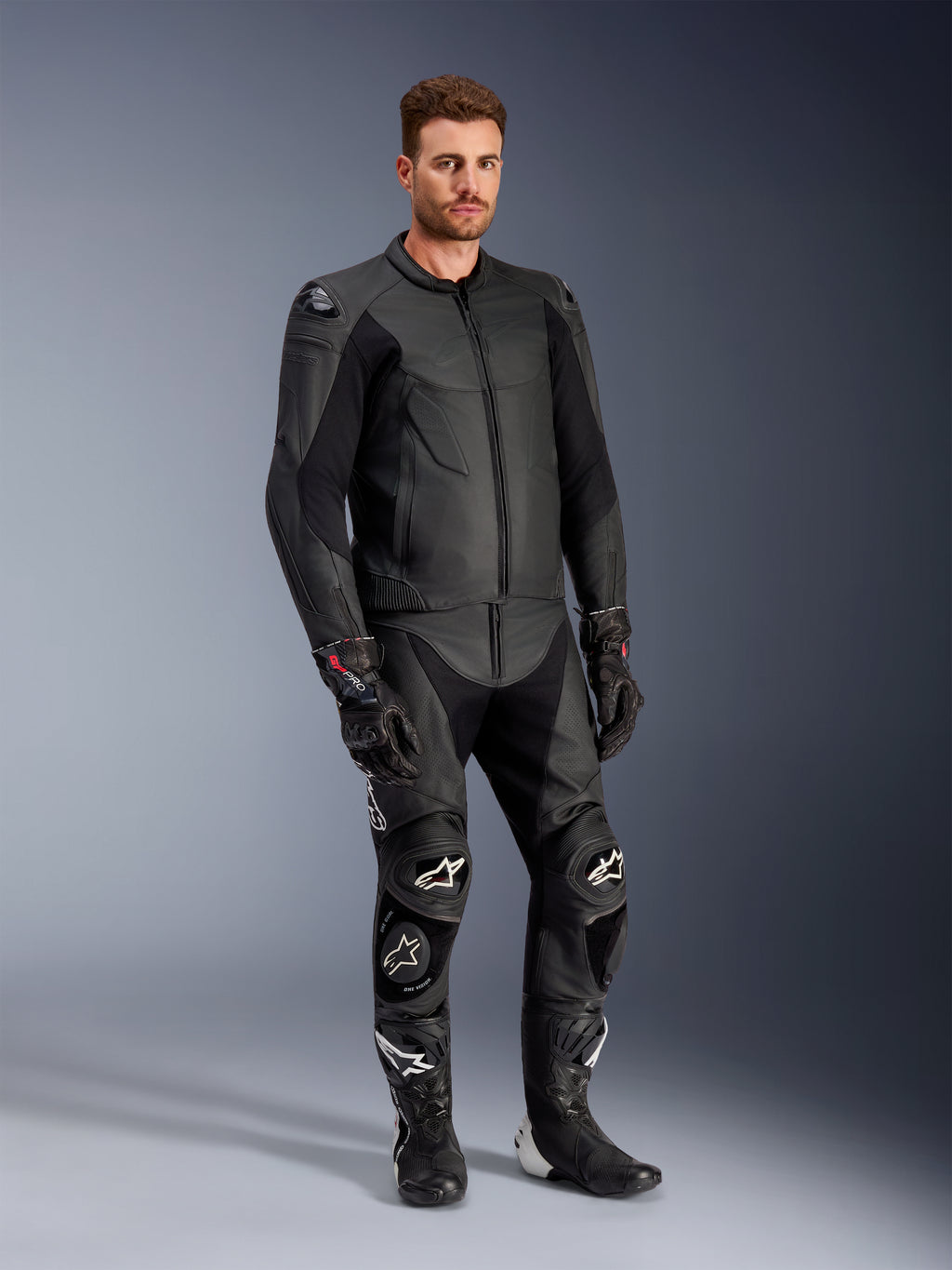Alpinestars Caliber leren jas in het zwart, gecombineerd met bijpassende zwarte leren motorbroek, racehandschoenen en laarzen, mannelijk model in een complete sportieve weguitrusting