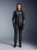 Alpinestars Stella Dusk leren damesjas, zwart en wit, gedragen door een model met bijpassende zwarte broek en laarzen, vooraanzicht, witte Alpinestars logo's op de borst en mouwen, premium runderleren beschermende kleding voor dames