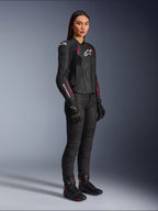 Alpinestars Stella Dusk leren damesjas, zwart met Diva roze en wit, gedragen door een vrouwelijk model met zwarte motorbroek en laarzen, voorzien van een strakke leren constructie met roze details en witte logo's