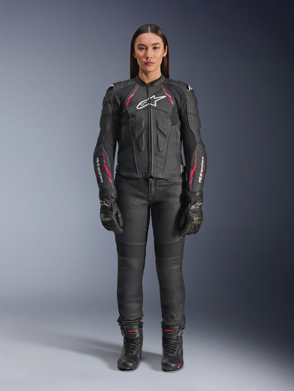 Alpinestars Stella Dusk leren jas, motorjas voor dames, Black Diva Pink White met wit logo op de borst en roze accenten op de schouders en mouwen, gecombineerd met zwarte motorbroek, handschoenen en laarzen, persoon draagt volledige motoruitrusting