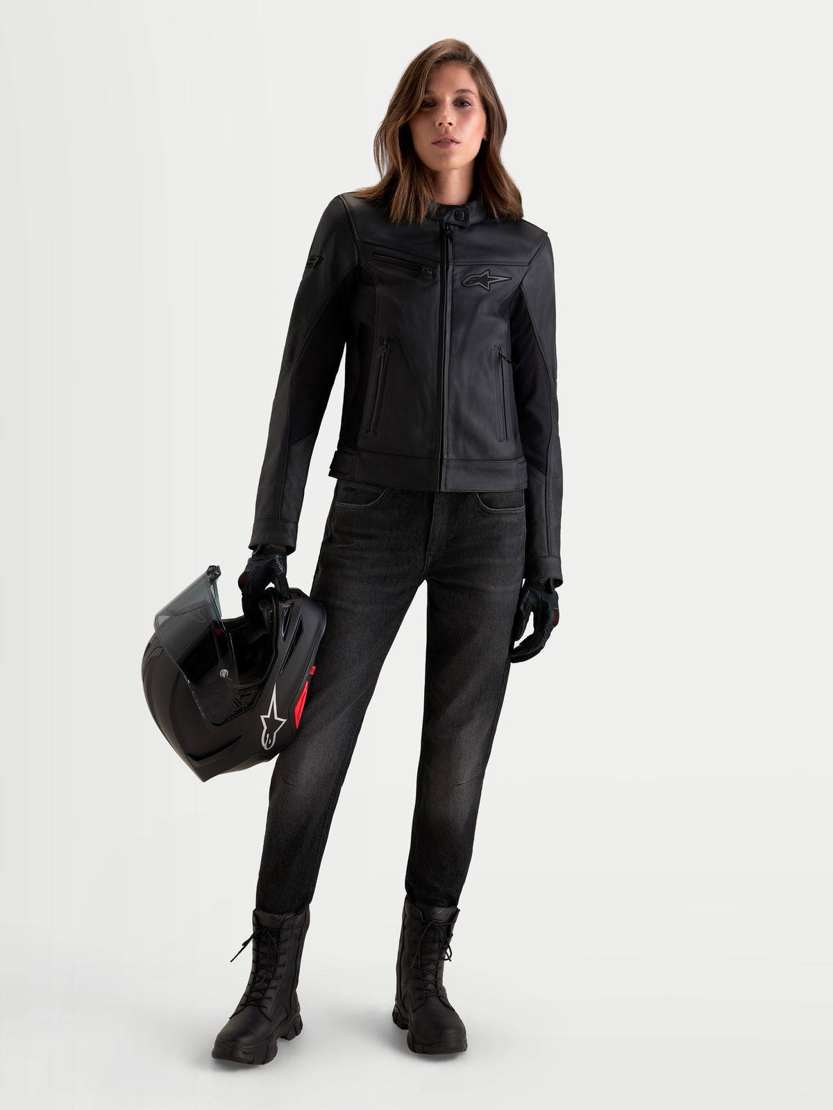 Alpinestars Stella Maver X leren jas, dames motorjas in het zwart, vooraanzicht van een model met de leren jas die een helm vasthoudt, met zachte rundleerconstructie