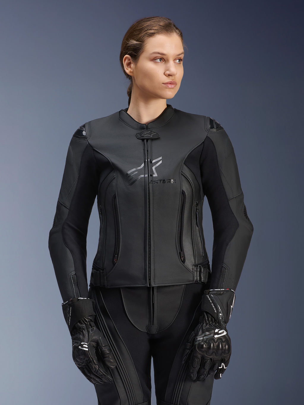 Alpinestars Stella GP Plus V4 leren jas, zwart, motorracejas voor dames, hoogwaardige leren constructie met beschermende vulling, strak ontwerp met subtiel logo, gedragen door een vrouwelijk model met bijpassende zwarte uitrusting