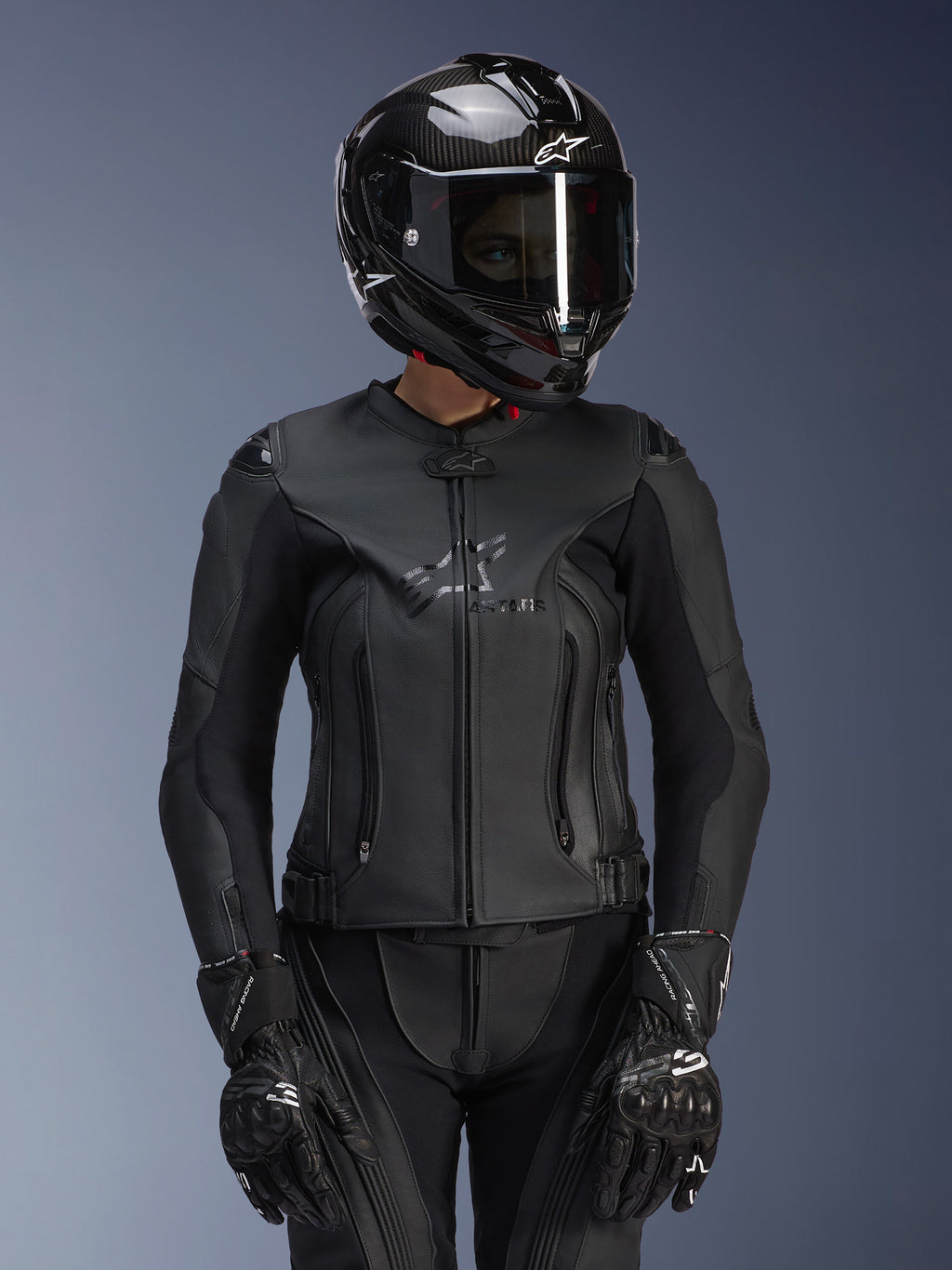 Alpinestars Stella GP Plus V4 leren damesjas in Black Black, gedragen met een zwarte carbon helm en racehandschoenen, slanke leren constructie met subtiele merknaam op de borst, getailleerd silhouet voor vrouwelijke rijders, professionele sportmotoruitrusting