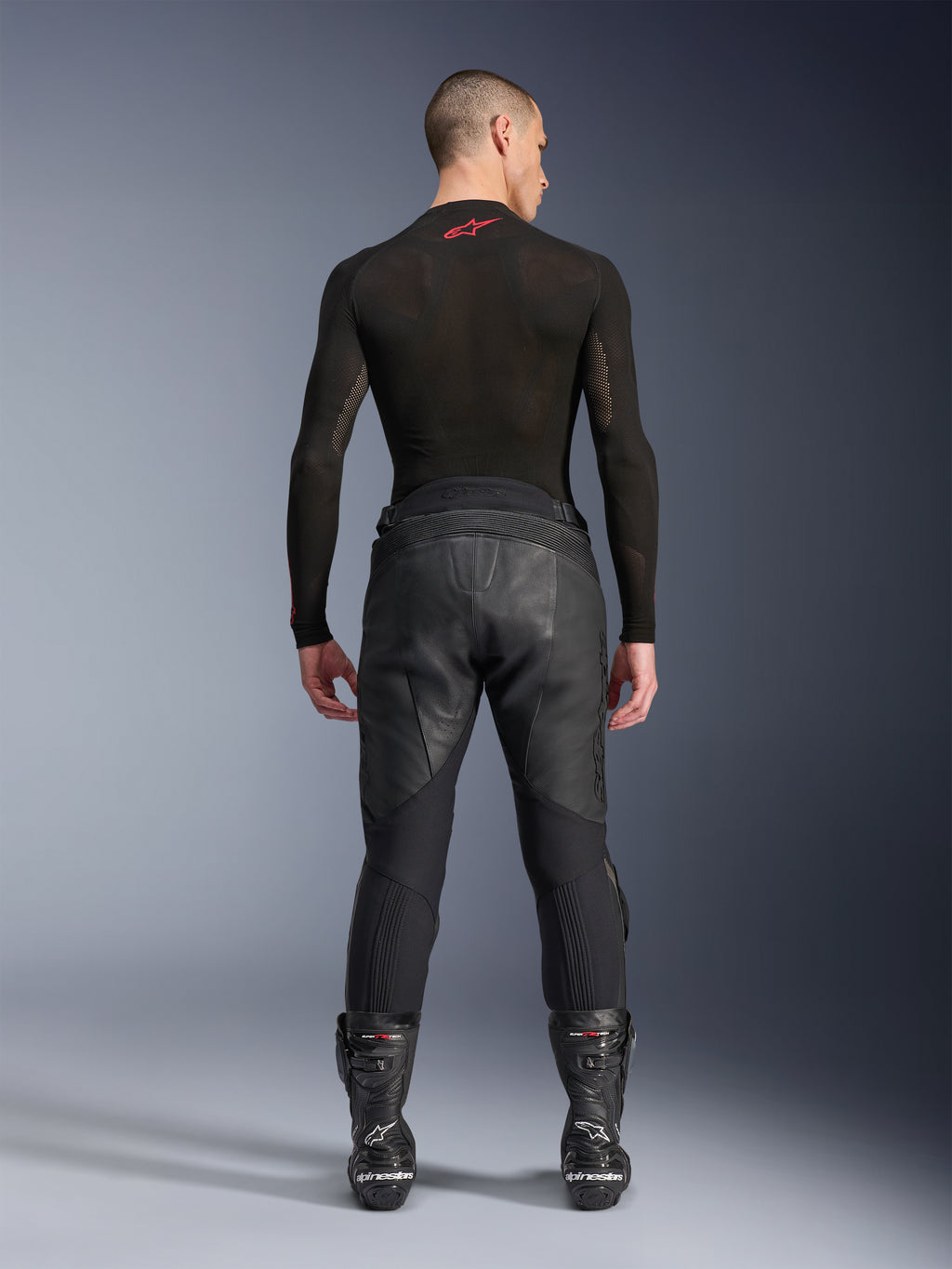 Alpinestars Missile V3 Leren Broek, zwart, achteraanzicht op model die een zwart compressieshirt met lange mouwen en racelaarzen draagt, premium leren constructie met hoge taille overlap en stretchzones, professionele motorrace-uitrusting