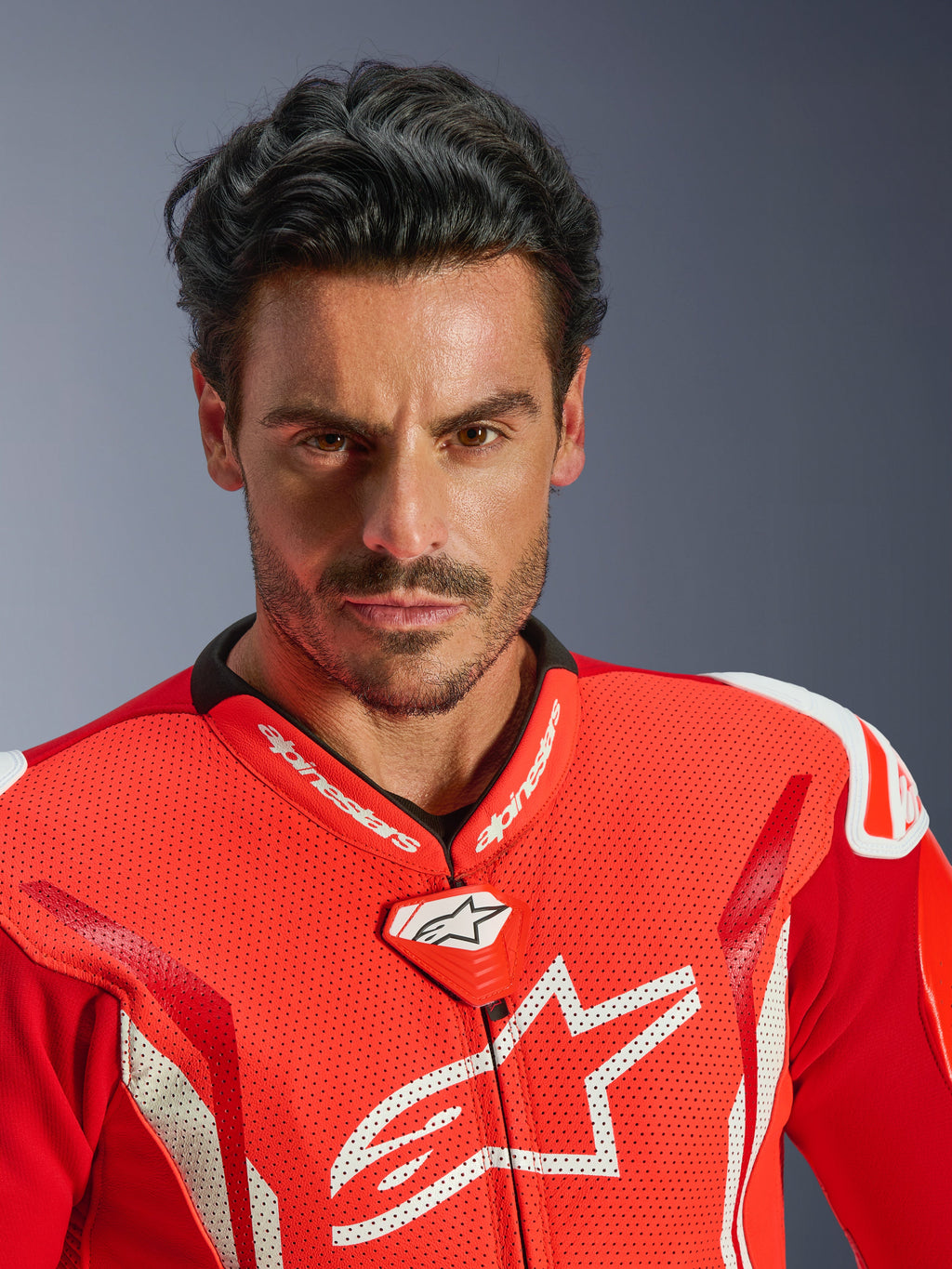Alpinestars GP Tech V5 eendelig leren pak, motorracepak, Red Fluo Bright Red en wit, close-up portret van een motorrijder, geperforeerde lederen borst met wit Alpinestars-logo, hoogwaardige racekraag en aerodynamisch ontwerp.