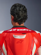 Close-up van de bovenrug en nek van het GP Tech V5 eendelig leren pak, Red Fluo en Bright Red, met wit Alpinestars-woordmerk op de kraag en GP TECH-logo op de aerodynamische bult, gedragen door een rijder.
