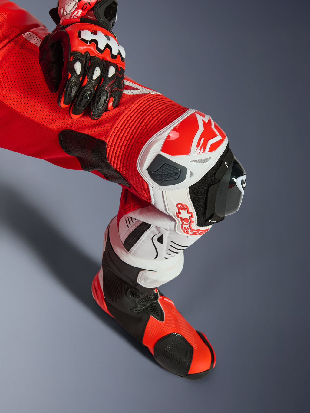 Alpinestars GP Tech V5 eendelig leren pak, Red Fluo Bright Red White, close-up van het been met kniebescherming en knieslider, voorzien van geperforeerd leer en accordeon stretchpanelen, gecombineerd met bijpassende racehandschoen en laars