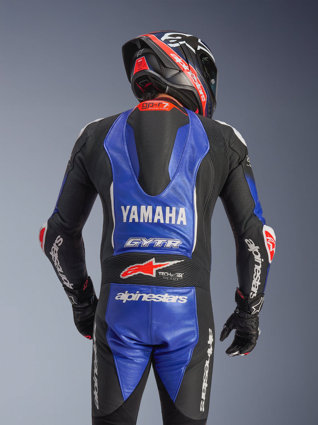 Alpinestars Yamaha GP-R7 eendelig leren motorpak, achteraanzicht, metallic blauw en zwart met witte en rode accenten, opvallende Yamaha- en GYTR-branding, aerodynamische speedbult, gedragen met bijpassende racehelm en handschoenen voor een professionele look op het circuit