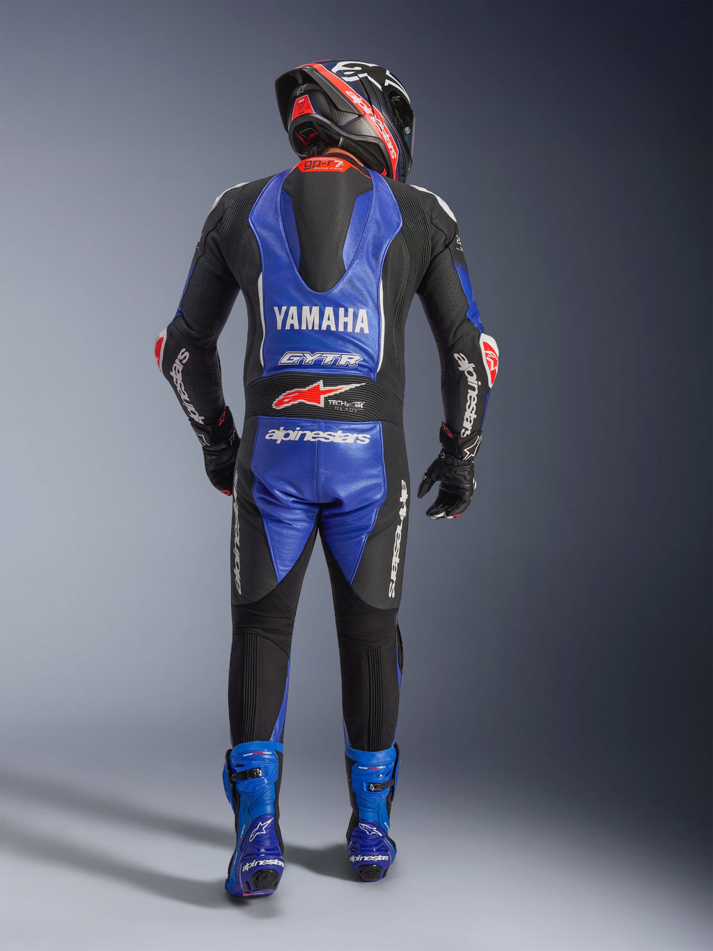 Alpinestars Yamaha GP-R7 eendelig leren pak, achteraanzicht van een motorrijder in volledige race-uitrusting, Metallic Blauw en Zwart met witte en rode accenten, Yamaha- en GYTR-branding op de aerodynamische bult, gedragen met bijpassende blauwe laarzen en een racehelm.