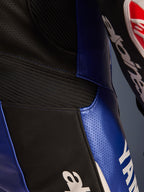 Detailopname van het Alpinestars Yamaha GP-R7 eendelig leren pak, metallic blauw en zwart, voorzien van geperforeerde leren panelen voor ventilatie, zwarte accordeon stretch-inzetten voor flexibiliteit en opvallende witte Yamaha-branding, wat de constructie van runderleer van racekwaliteit benadrukt.
