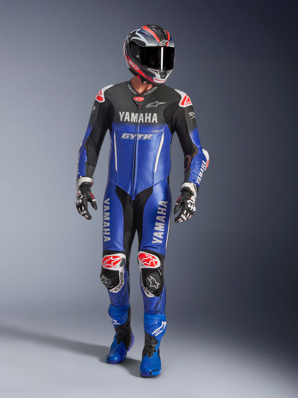 Alpinestars Yamaha GP-R7 eendelig leren racepak, motorracepak, metallic blauw en zwart met rode en witte accenten, voorzien van Yamaha- en GYTR-branding, gedragen met bijpassende helm, racehandschoenen en blauwe laarzen, professionele performance uitrusting