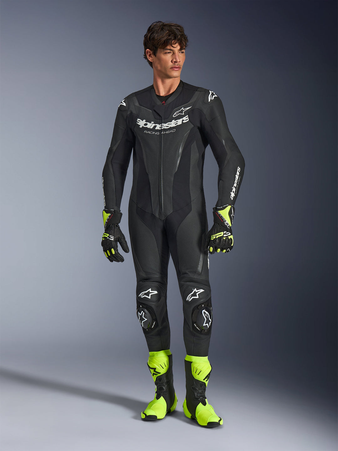 Alpinestars GP Force V2 lederen pak, eendelig zwart motorracepak, gedragen met fluorescerend gele laarzen en handschoenen, voorzien van witte logo's en geperforeerd leer, nauwsluitend ontwerp voor circuitdagen