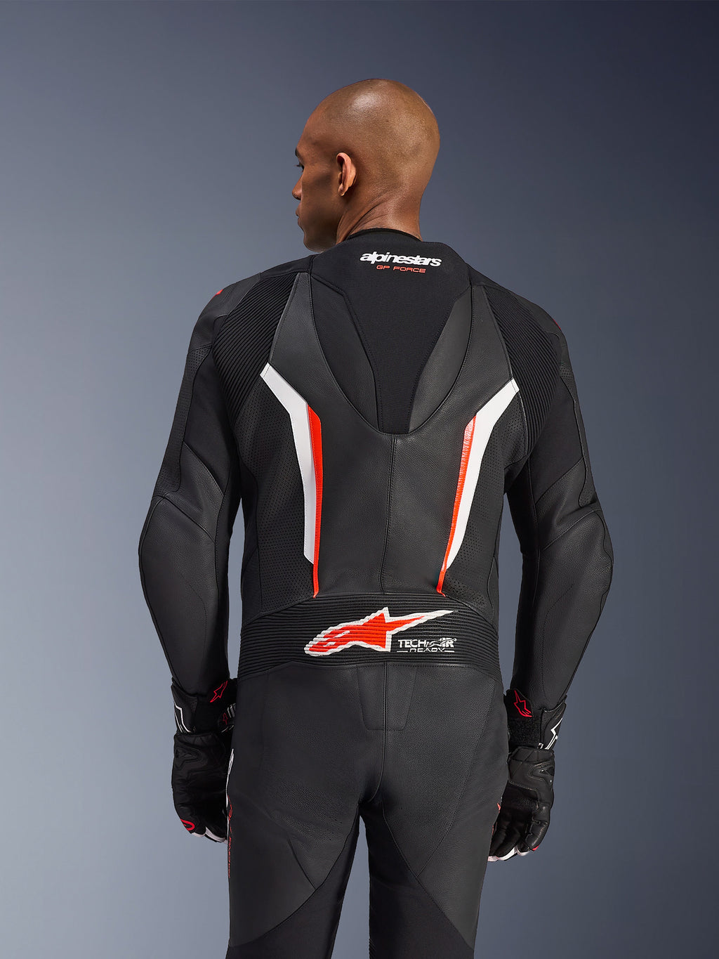 Alpinestars GP Force V2 leren pak, 1-delig motorpak, zwart, wit en fluo rood, achteraanzicht van het bovenlichaam met geperforeerd leer en Tech-Air Ready-logo, gedragen met bijpassende zwart-rode handschoenen