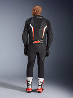 Achteraanzicht van een model in het Alpinestars GP Force V2 1-delig leren pak in Black White Red Fluo, met de aerodynamische speedhump en Tech-Air Ready-branding, gecombineerd met wit-rode professionele racelaarzen en zwarte handschoenen.