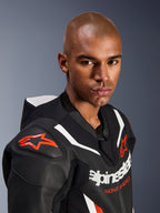 Close-up portret van een model dat het Alpinestars GP Force V2 leren pak draagt, 1-delig, zwart wit en fluo rood, voorzien van geperforeerde leren panelen, witte racestrepen en rode Alpinestars-logo's op de schouder en borst.
