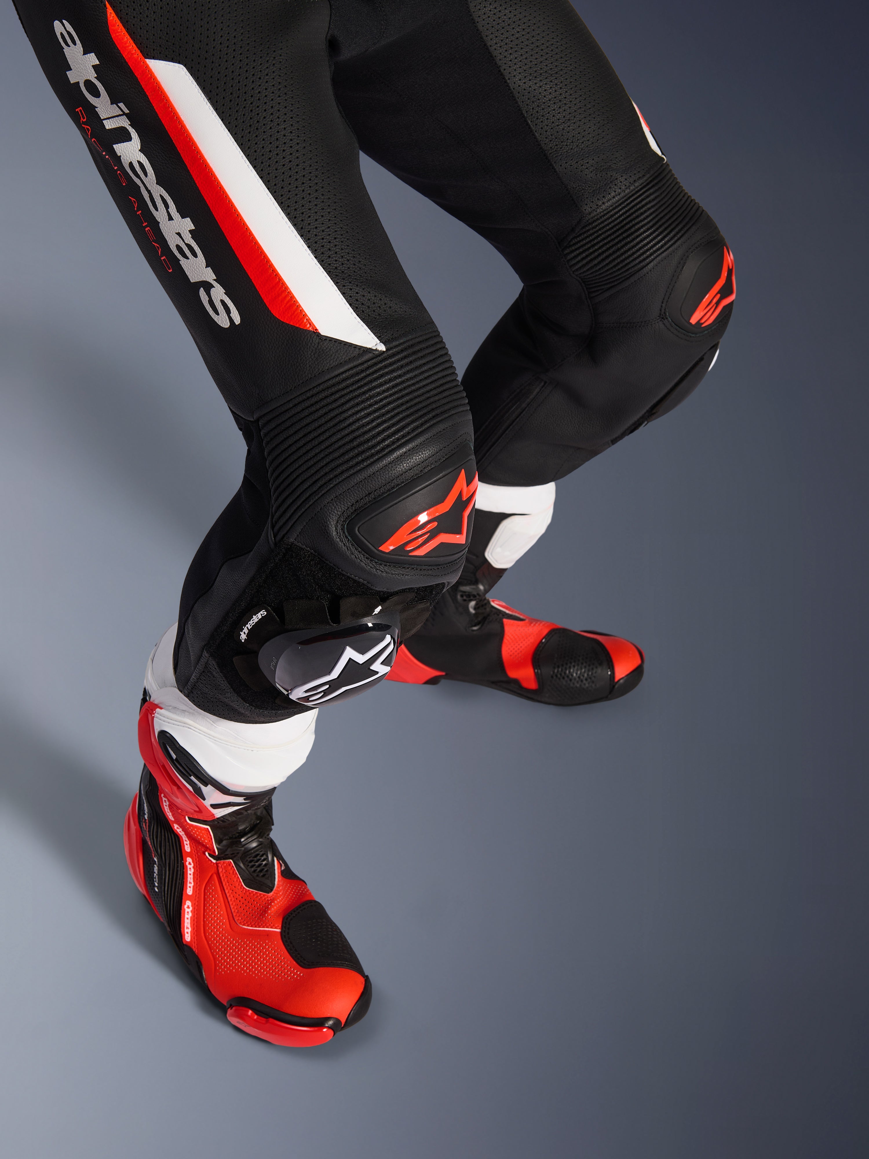 Alpinestars GP Force V2 1-delig leren pak, zwart, wit en fluo rood, close-up van de onderbenen en knieën met DFS Lite-protectoren en vervangbare sliders, gecombineerd met professionele racelaarzen