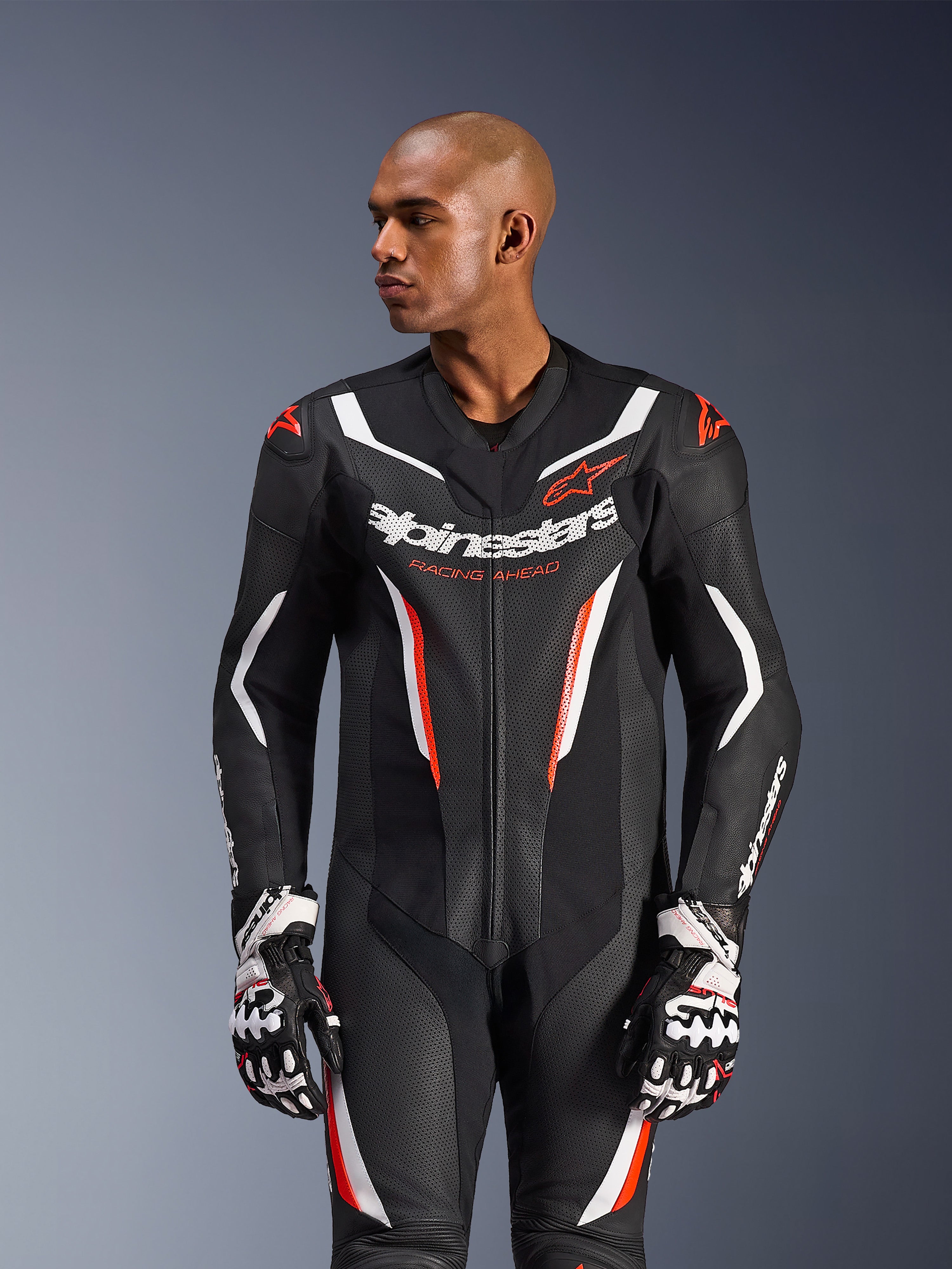 Alpinestars GP Force V2 1-delig leren pak, zwart wit rood fluo, gedragen door een mannelijk model met racehandschoenen, voorzien van een geperforeerde leren constructie, opvallende witte en rode grafische accenten en Alpinestars-branding op de borst.