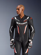 Alpinestars GP Force V2 Leren Pak - 1-delig, motorracepak, zwart, wit en fluo rood, met geperforeerde leren panelen, opvallende merkdetails op de borst met de tekst 'Racing Ahead' en een ergonomisch beschermend ontwerp, gedragen met bijpassende racehandschoenen