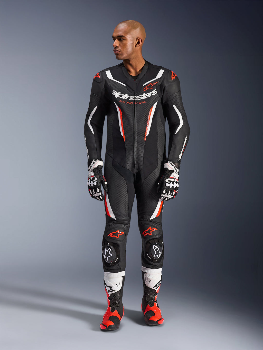 Alpinestars GP Force V2 Leather Suit - 1Piece, zwart wit en rood fluo, volledige weergave van mannelijk model in professionele motorrace-uitrusting met bijpassende handschoenen en laarzen, voorzien van geperforeerde leren panelen en beschermende kniesliders.