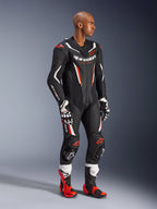 Model draagt het Alpinestars GP Force V2 1-delig leren pak in Black White Red Fluo, hoogwaardige race-uitrusting met geperforeerde leren panelen en DFS Lite-schilden, gecombineerd met bijpassende rood-witte racelaarzen en handschoenen, professionele motorsport-uitstraling.