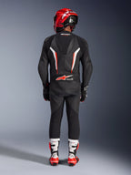 Rijder van achteren gezien in het Alpinestars GP Force V2 1-delig leren pak in Black White Red Fluo, voorzien van een aerodynamische speedhump en Tech-Air Ready branding, gecombineerd met een rode racehelm en wit-rode laarzen, professioneel circuituitrusting ontwerp.