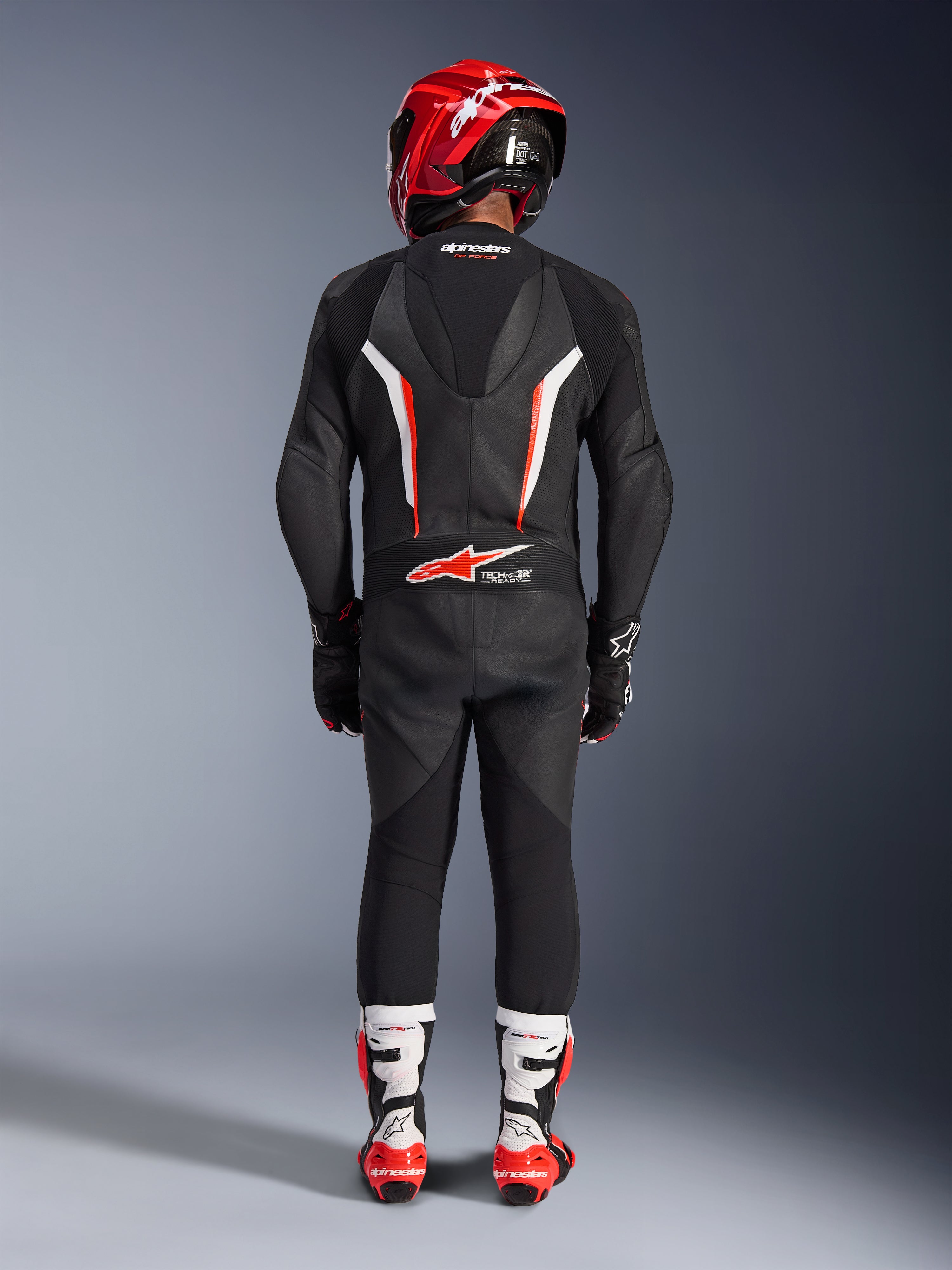 Rijder van achteren gezien in het Alpinestars GP Force V2 1-delig leren pak in Black White Red Fluo, voorzien van een aerodynamische speedhump en Tech-Air Ready branding, gecombineerd met een rode racehelm en wit-rode laarzen, professioneel circuituitrusting ontwerp.