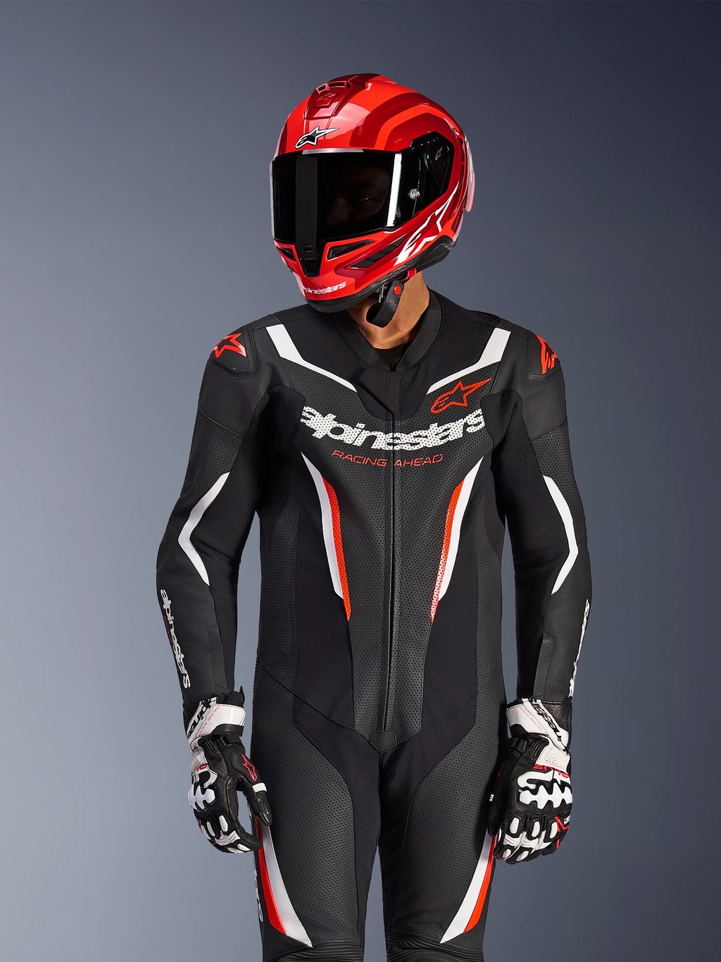 Motorrijder in Alpinestars GP Force V2 eendelig leren pak in Zwart Wit Rood Fluo, bijpassende rode racehelm en handschoenen, voorzien van geperforeerde lederen panelen en opvallende branding, hoogwaardige race-uitrusting