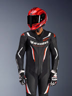 Motorrijder in Alpinestars GP Force V2 eendelig leren pak in Zwart Wit Rood Fluo, bijpassende rode racehelm en handschoenen, voorzien van geperforeerde lederen panelen en opvallende branding, hoogwaardige race-uitrusting
