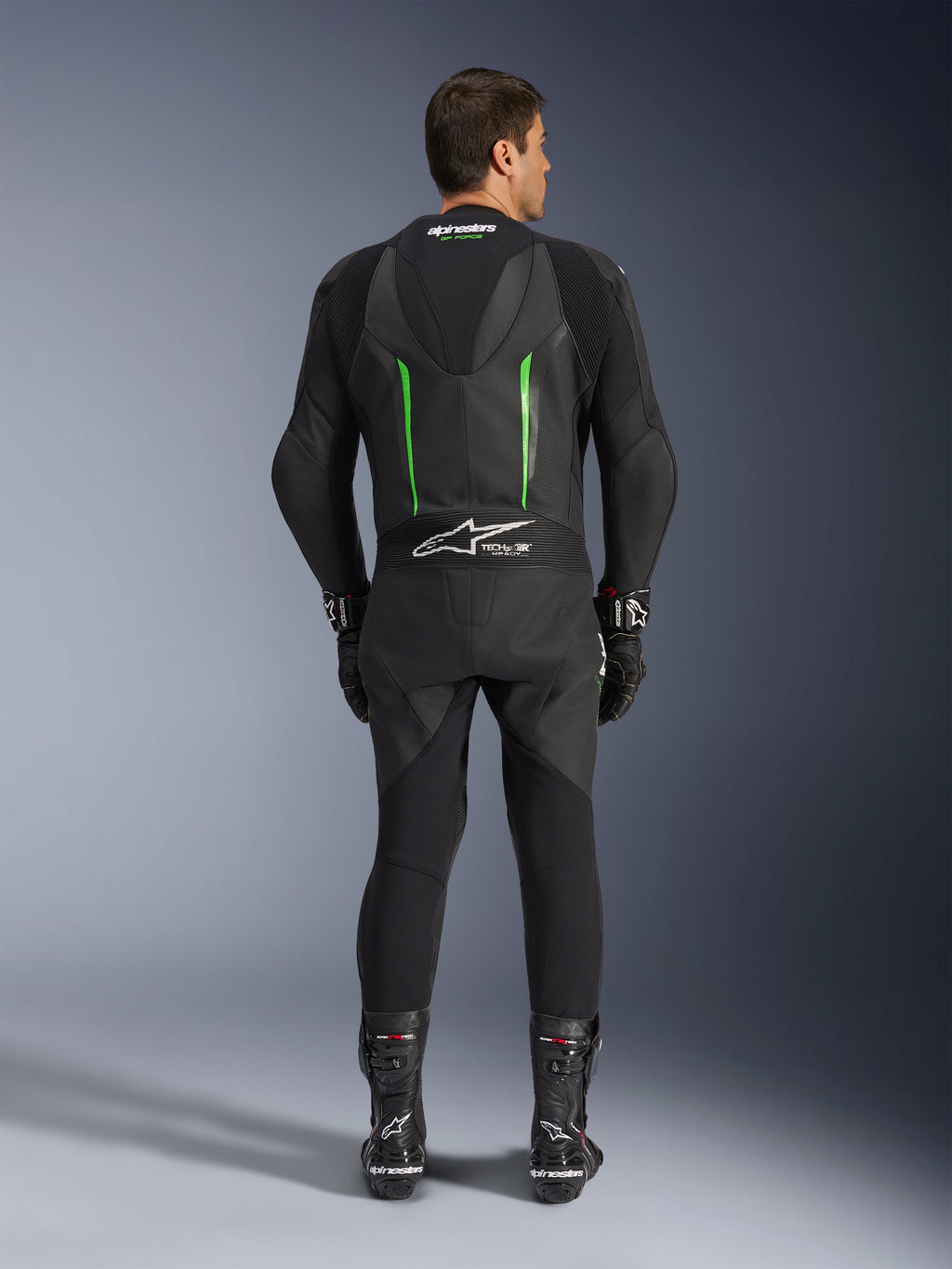 Achteraanzicht van het Alpinestars GP Force V2 1-delig leren pak in zwart en groen, voorzien van een aerodynamische speed hump, geperforeerde panelen en Tech-Air Ready-branding op de onderrug, gedragen met zwarte racehandschoenen en laarzen.