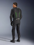 Alpinestars GP Force V2 Leren Pak, 1-delig motorpak, zwart met groene accenten, achteraanzicht met de aerodynamische speed hump en wit logo op het accordeon stretchpaneel, gecombineerd met zwarte racelaarzen en handschoenen.